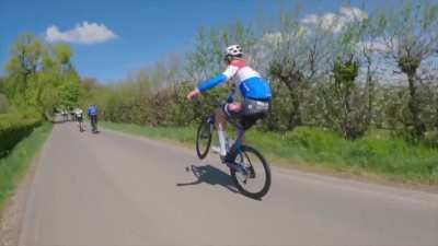 A pro cyclist casually passes other riders while doing a wheelie