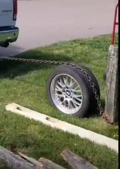 Pulling a post from the ground with a chain wrapped around a car wheel