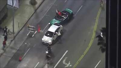 Protesters chase a vehicle down, smash the windows with a skateboard while attempting to pull the driver out of the car. After speeding away the driver is being handcuffed by LAPD