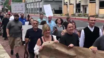Anti-mask protesters march around the Indiana State House chanting “USA” and “We Will Not Comply