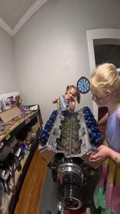 Two little girls helping their dad build an engine
