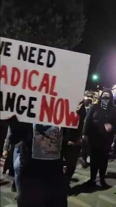 Black bloc anarchists surround Chad Nesbitt (a reporter for Skyline News in Asheville NC) before pushing another man into him, knocking him out and giving him a traumatic brain injury. He was taken away in an ambulance.