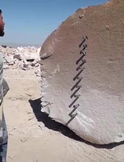Man splitting a huge rock open with a hammer and some stakes