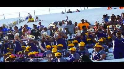 Trombone section and soloist surprise their own band with a new rendition of a song during a football game. 1 by 1, you can pinpoint when each bandmate realizes that they are listening to a legendary performance until they all explode with amazement