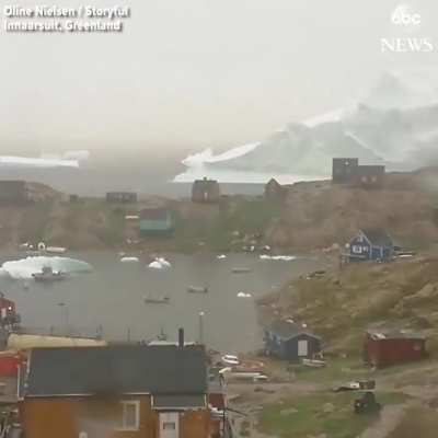 Iceberg casually drifting past a village in Greenland