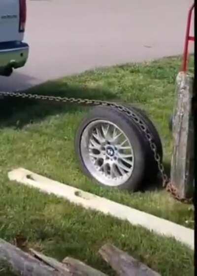 Pulling a post from the ground with a chain wrapped around a car wheel