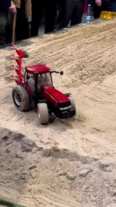 A remote control tractor tilling a small field.