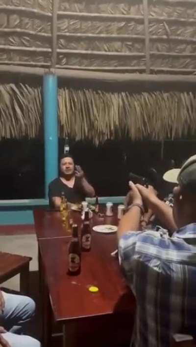 Man shoots a bottle off his friend's head.