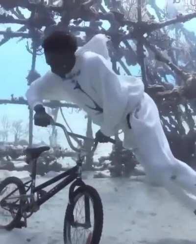 A guy takes his diving gear off to take a photo with his BMX bike at the bottom of the ocean