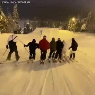 Seven skiers hold hands and flip in unison