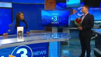 TV presenter cheerfully taken aback as she reads about her relationship to her colleague from the teleprompter and then surprised with a proposal from him