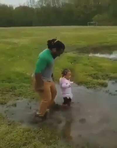Dad jumps in puddle of water with his daughter. It’s the little things that make kids happy.