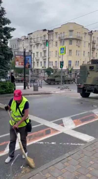 Ru pov: A city worker continues her work, in the background Alleged military personnel and hardware from the WAGNER PMC in Rostov