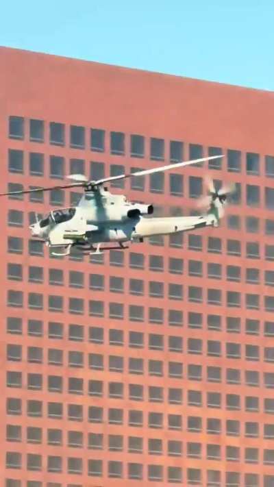 A U.S. Marine Corps AH-1Z Viper attack helicopter flies low over downtown Los Angeles, signaling a possible military deployment amid ongoing unrest.