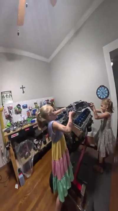 Two little girls helping their dad rebuild an engine