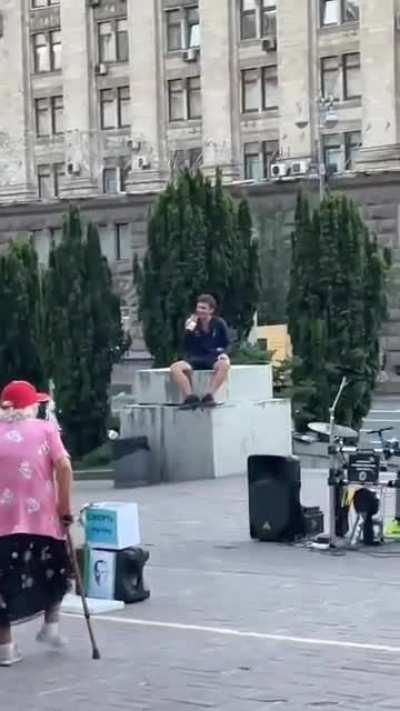 A Ukrainian grandma is enjoying her life while young guys playing music in support of Armed Forces of Ukraine