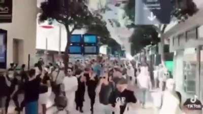 A human wave of protesters refusing to wear a mask or show their papers overwhelm the police and shout, 