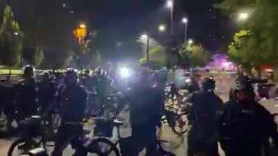 Man intentionally lays down in the road twice as Seattle police advance. First time they ride right by him, but the second time an officer walks his bike over the guy's hardhat.