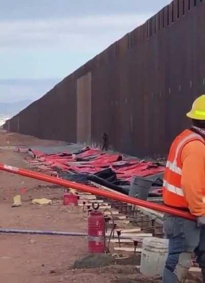 Man scaling the US-Mexican Border… with workers present