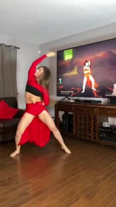 A girl in a red outfit dances enthusiastically in front of a television with a video of a similar girl. That is all.