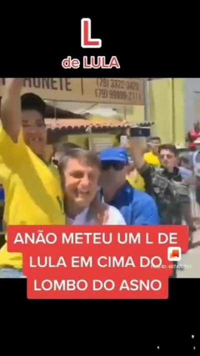 Bolsonaro ergue um homem com nanismo vestido de amarelo durante sua campanha. O homem, sobre os ombros de Bolsonaro, faz o L de Lula para a multidão.