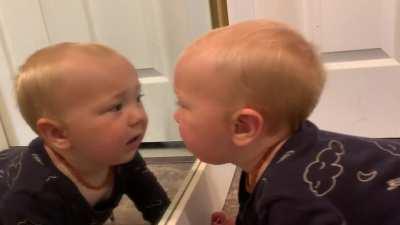 Baby fights with his reflection from the mirror.