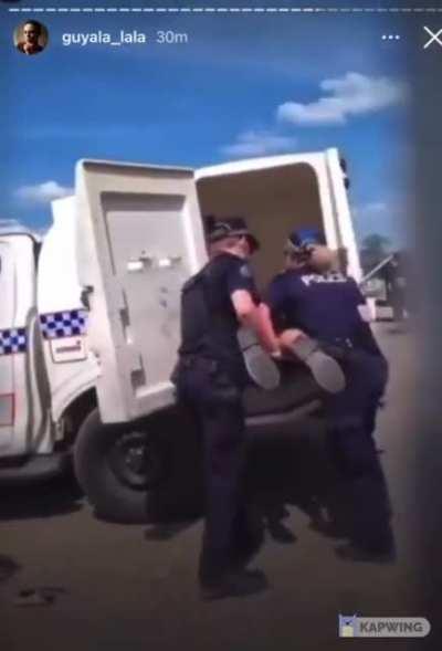 Two Australian police officers forcibly carry and push an indigenous elder into a vehicle to be transported to a 