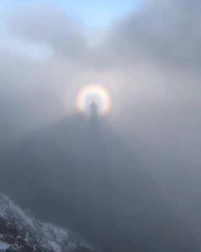 🔥 A hiker captures his own shadow floating in the mountain mist, surrounded by a glowing solar halo