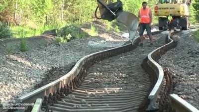 Straightening buckled railway tracks with an excavator