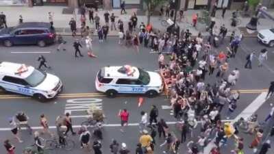 Overhead view of NYPD officers running over protesters who are behind a barrier