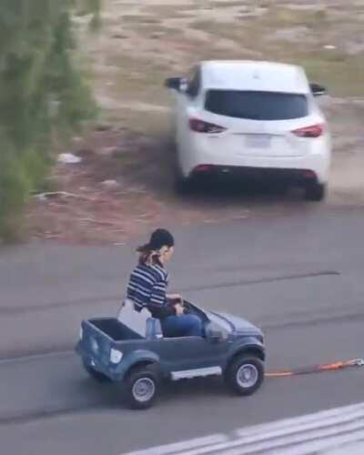 Towing a toy car with a person in it on the street at a high speed