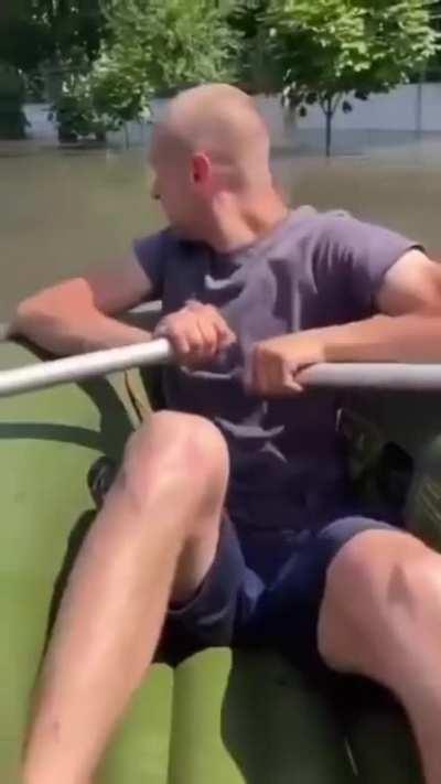 Ukrainian civilians in a flooded part of Kherson searching for people while there's shelling by the Russian military in the background