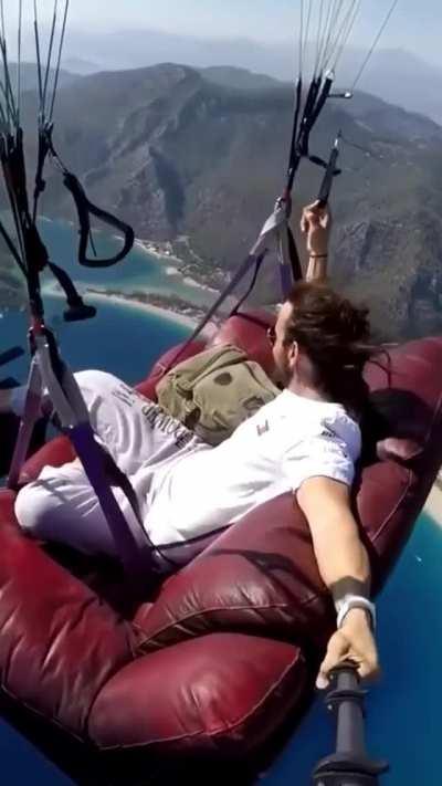 Parachutes on a couch while not wearing a parachute himself and no safety strap-in
