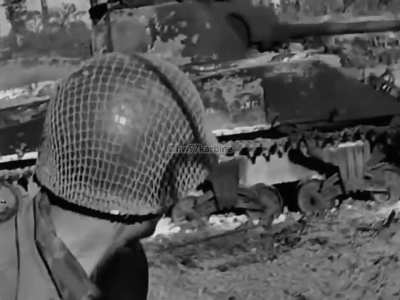 US 2nd Armored Division troops drive past a burned out Sherman tank in Normandy on July 26th 1944