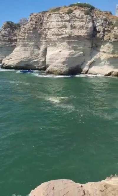 Man Cliff diving while Boats pass underneath