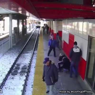 A boy pushes a lady onto the train tracks.