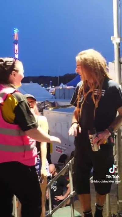A lady working concert security tries to stop a guy walking backstage, not realising its Lamb of God vocalist, Randy Blythe. He's a complete gentleman about it.