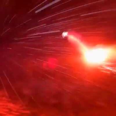 Man wingsuits off a mountain in a blizzard with a road flare at night.