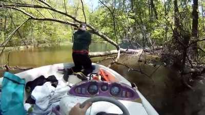 Steve using a chainsaw to clear branches while standing on a boat