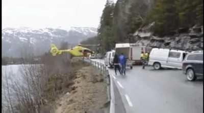 Helicopter balances on road railing to let off an emergency physician after car accident in Norway