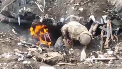 Russian soldier climbs out of a burning hole and collapses after a Ukrainian drone dropped an explosive inside. His comrade is on fire next to him.