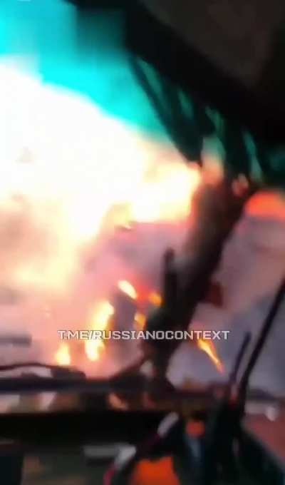 First-person footage of a Russian soldier driving by a truck transporting ammunition right at the moment it is exploding after getting hit by a Ukrainian FPV quad.