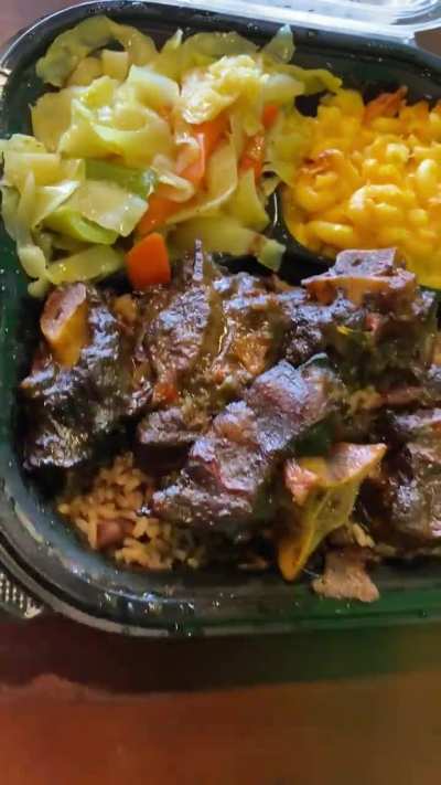 Jamaican oxtail on jollof rice with mac and cheese and cabbage.