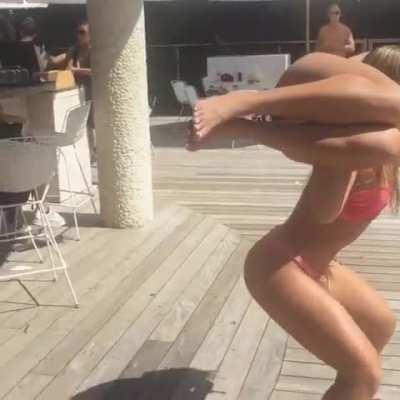 Girl in bikini weightlifts her prostrate friend