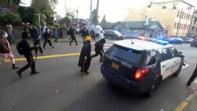 Portland Red House (#7): Antifa militant runs up to retreating cop car and throws tire-popping caltrops under it