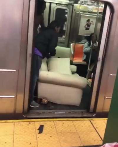 Guys loading a couch onto a subway train in NYC.