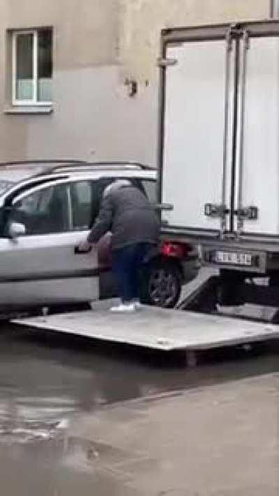 Guys use a lift gate on a truck to help a senior get into her car without getting her feet wet