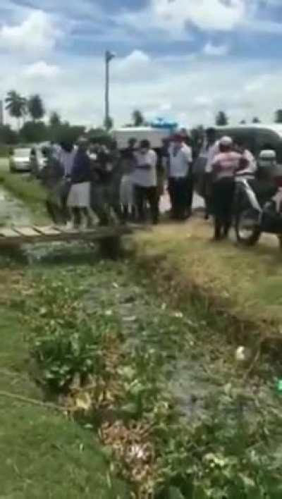 A lot of people crossing a little bridge with a dead body