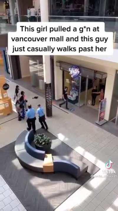 A guy with too little fucks to give walks past a woman who is threatening people with a gun