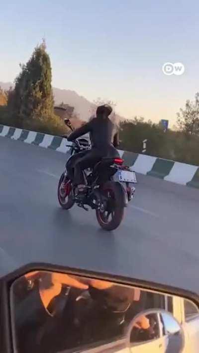 A woman is seen riding a motorbike without hijab. Breaking two rules.